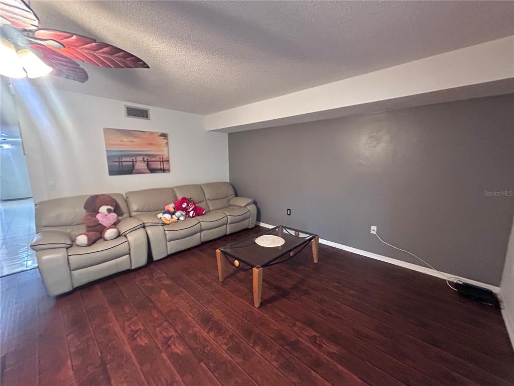 A living room features a light-colored sectional sofa, a glass coffee table, and dark flooring — 150 EL DORADO UNIT 208, WINTER HAVEN, FL
