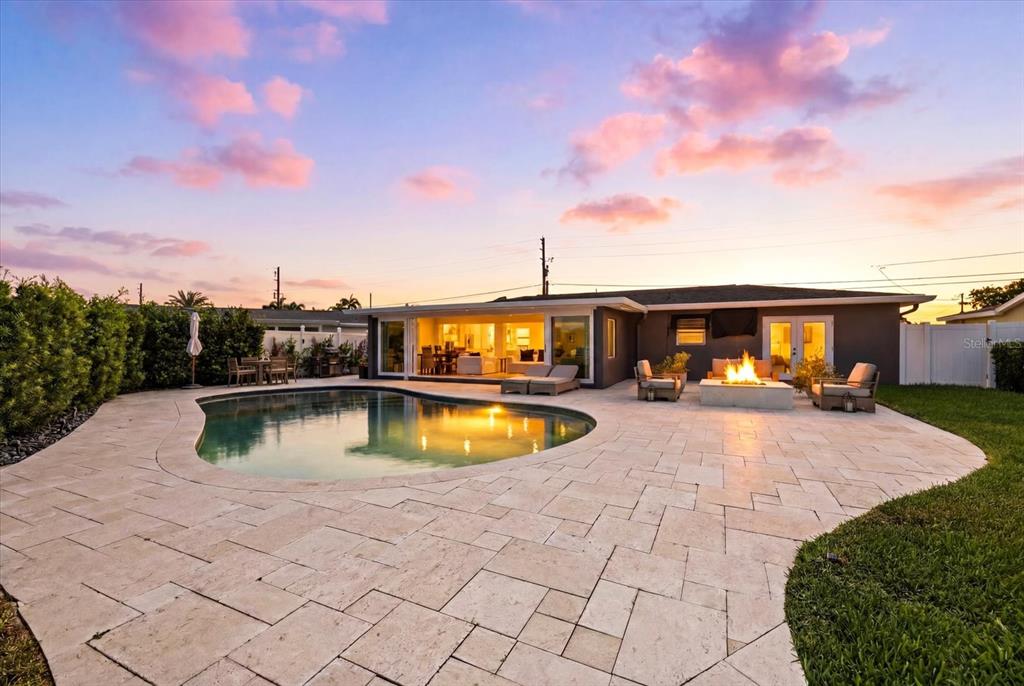 A backyard features a swimming pool, stone patio, fire pit, and a house at sunset — 121 79TH STREET S, ST PETERSBURG, FL