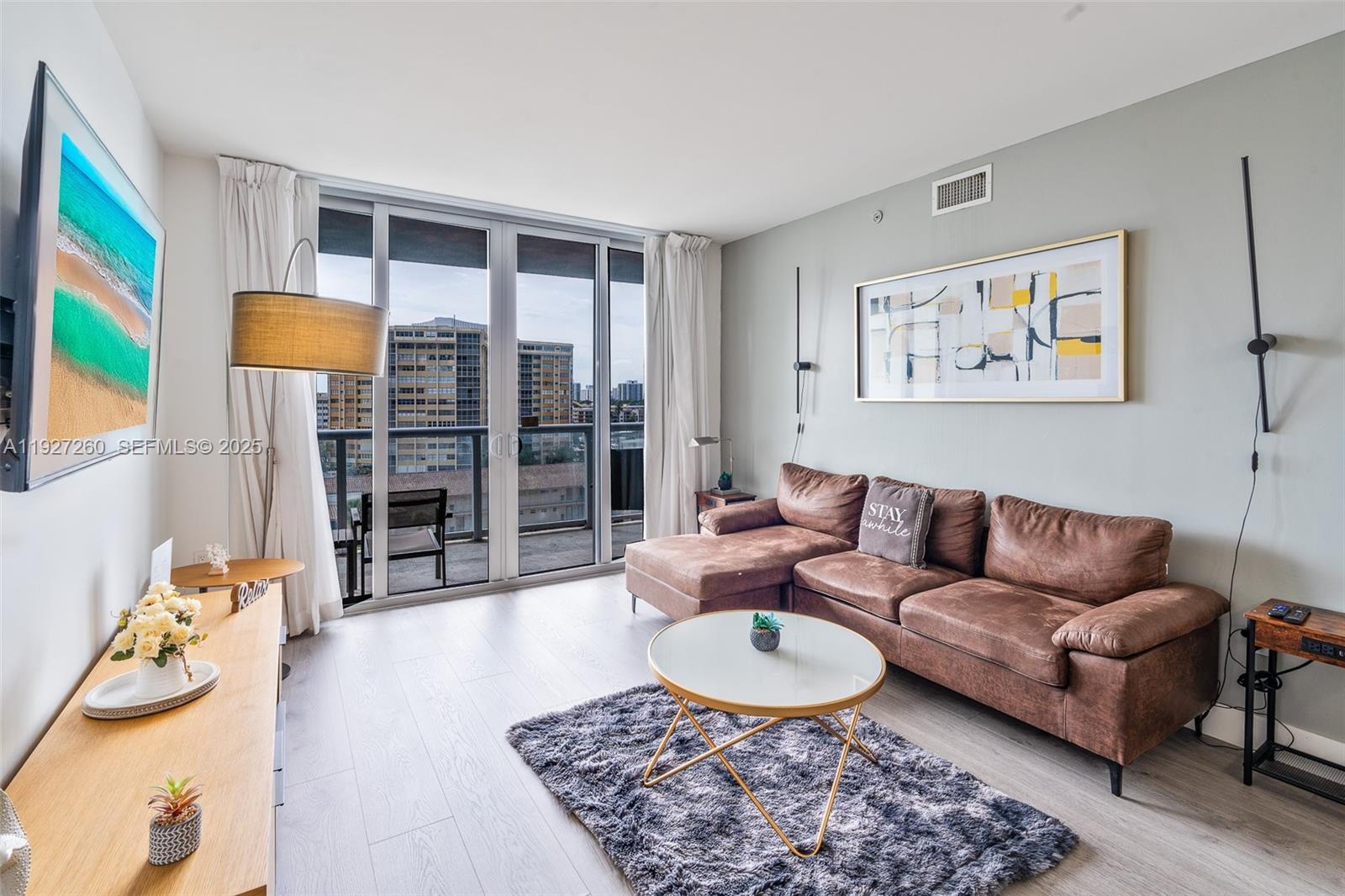 A living room features a brown sectional sofa, a round coffee table, and a balcony view — 2602 E Hallandale Beach Blvd # R809, Hallandale Beach FL 33009, HALLANDALE BEACH, FL