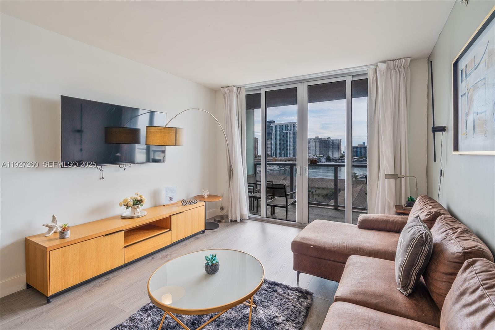 A living room features a brown sectional sofa, a wooden media console, and a balcony — 2602 E Hallandale Beach Blvd # R809, Hallandale Beach FL 33009, HALLANDALE BEACH, FL
