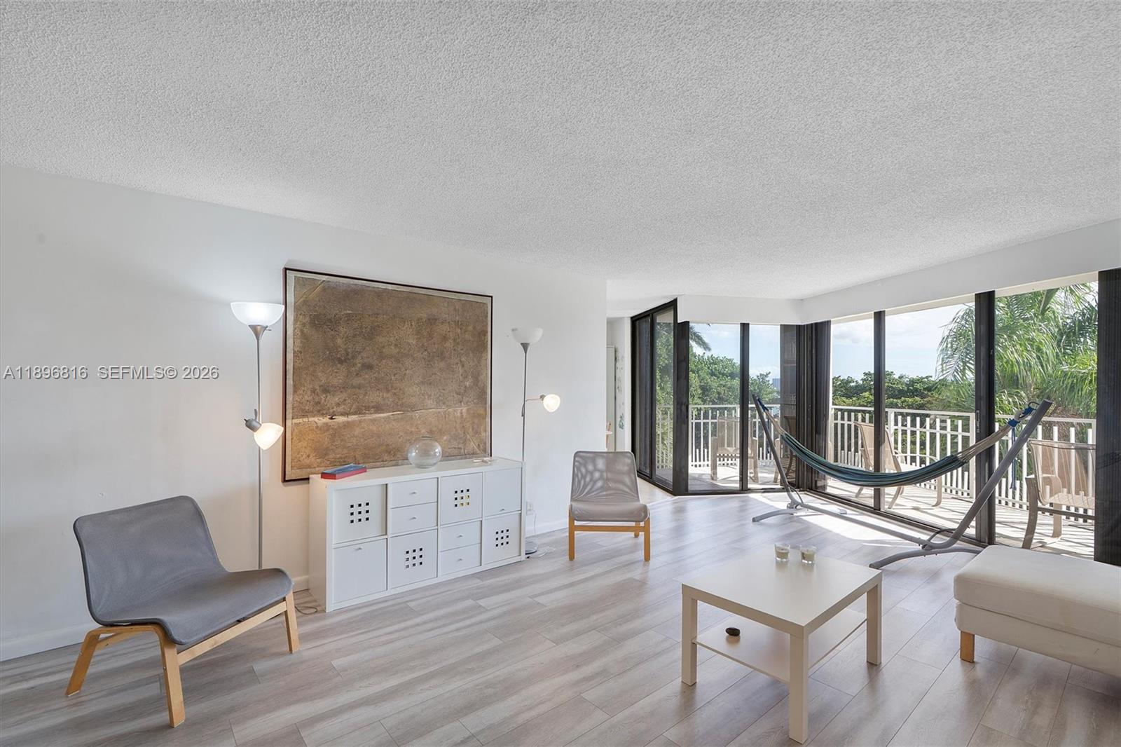 A living room features light wood-look flooring, a white storage unit, and a balcony view — 4000 Towerside Ter # 402, Miami FL 33138, MIAMI, FL