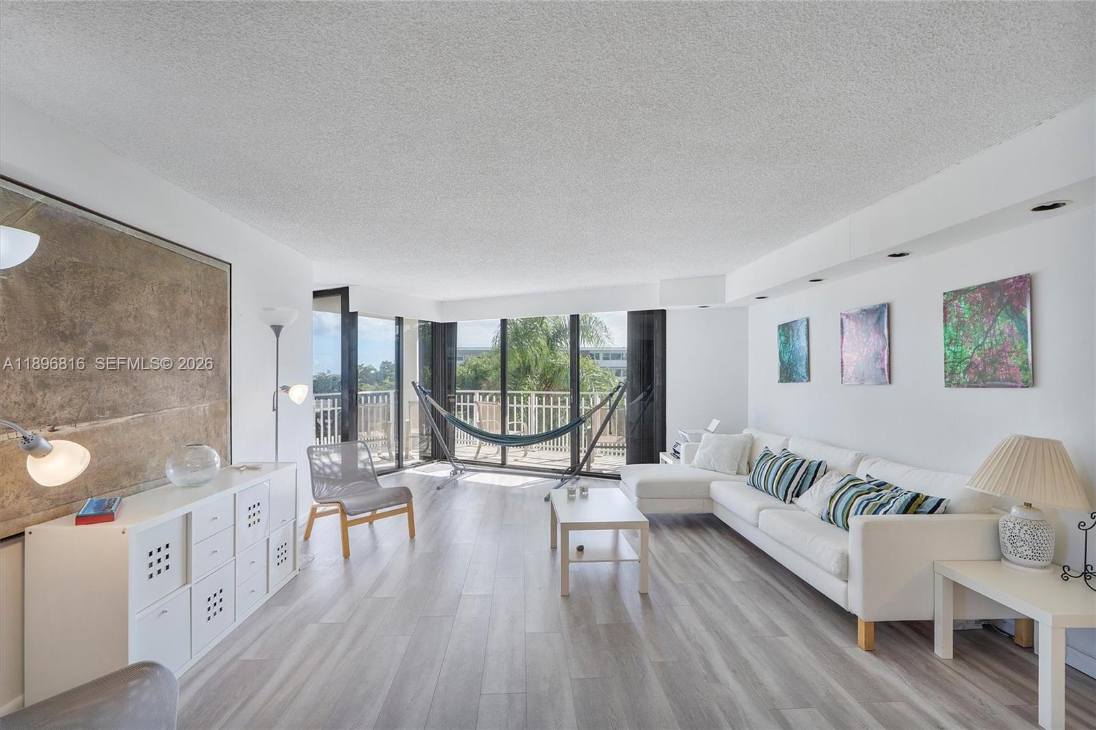 A bright living room features white walls, light wood-look flooring, a sectional sofa, and a hammock — 4000 Towerside Ter # 402, Miami FL 33138, MIAMI, FL