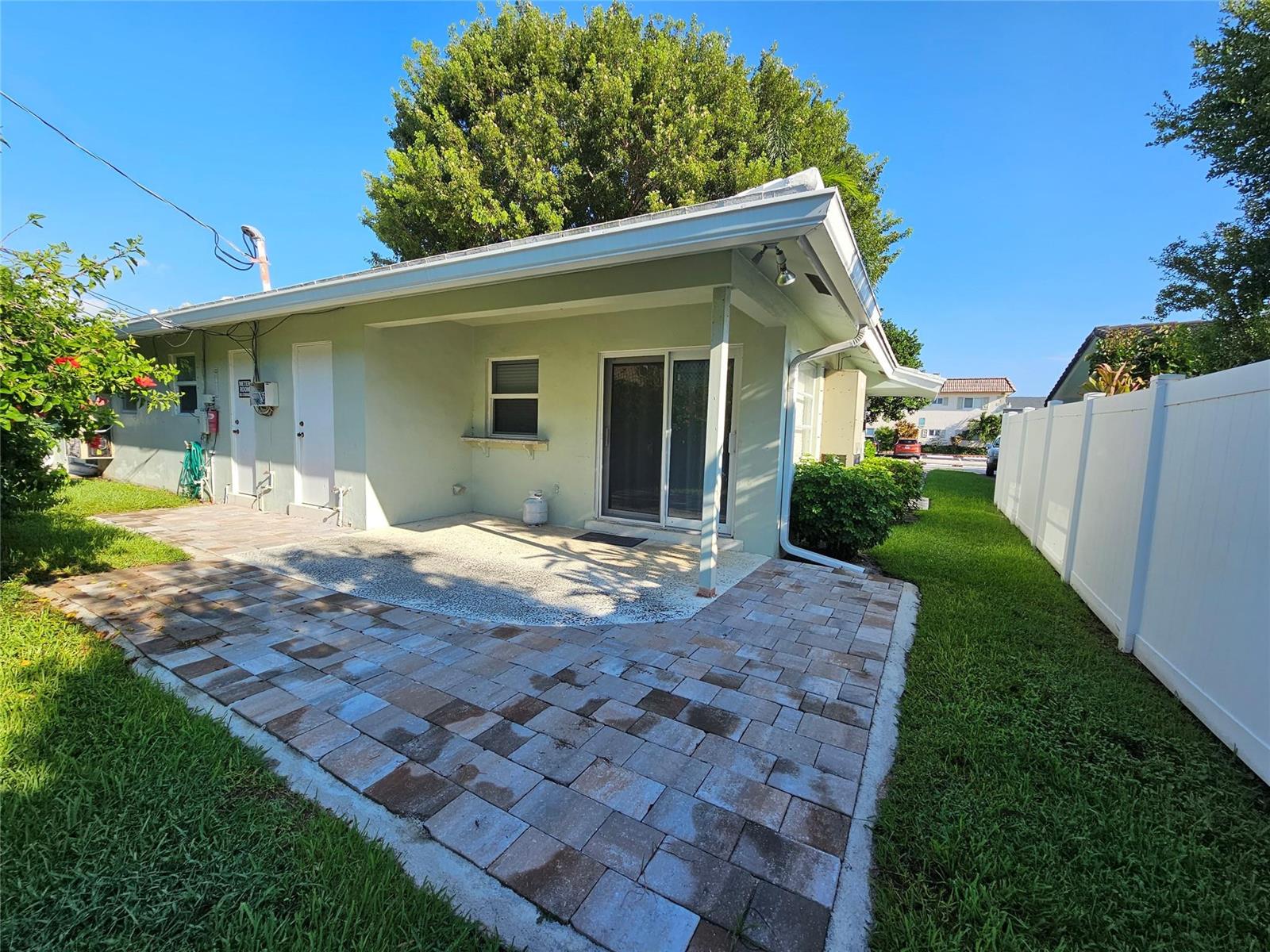 A light green house exterior features a paved patio, sliding glass doors, and a white fence — 2120 NE 41st Street # D, Lighthouse Point FL 33064, LIGHTHOUSE POINT, FL