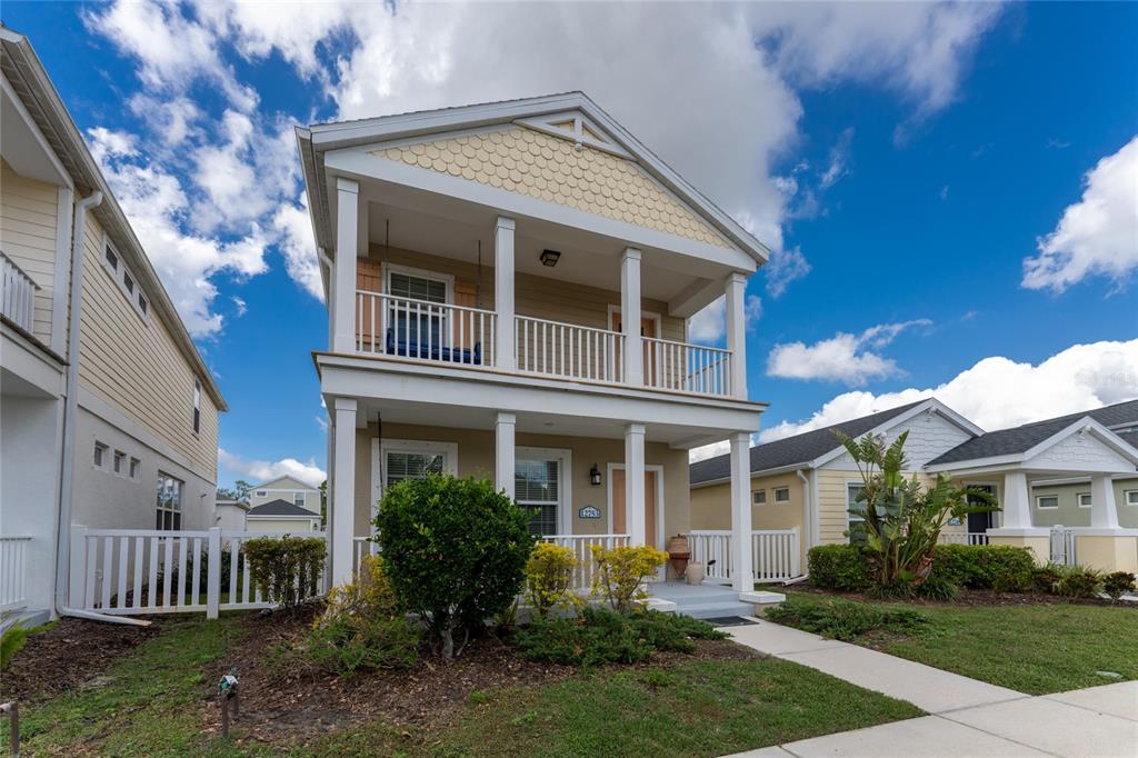 A two-story house with a front porch, balcony, and beige siding under a cloudy sky — 12753 SAGEWOOD DRIVE, VENICE, FL