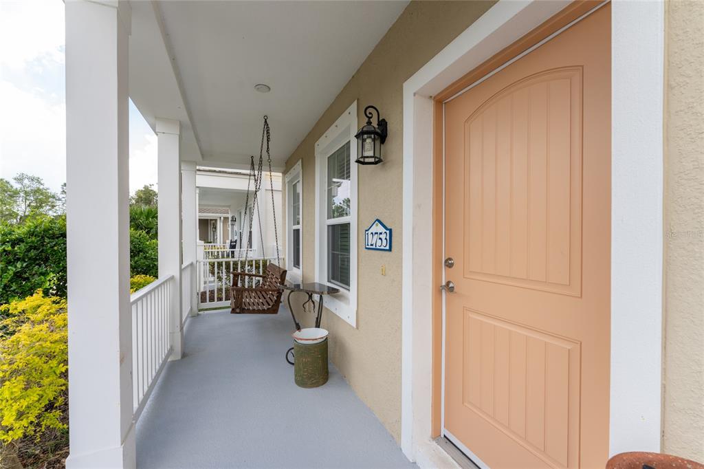 A covered front porch features a hanging wooden swing, a small table, and a peach-colored door — 12753 SAGEWOOD DRIVE, VENICE, FL