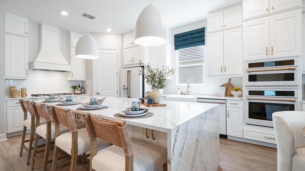 A bright kitchen features white cabinetry, a large marble-topped island, and modern pendant lighting — 7420 MOONBEAM AVENUE, SARASOTA, FL