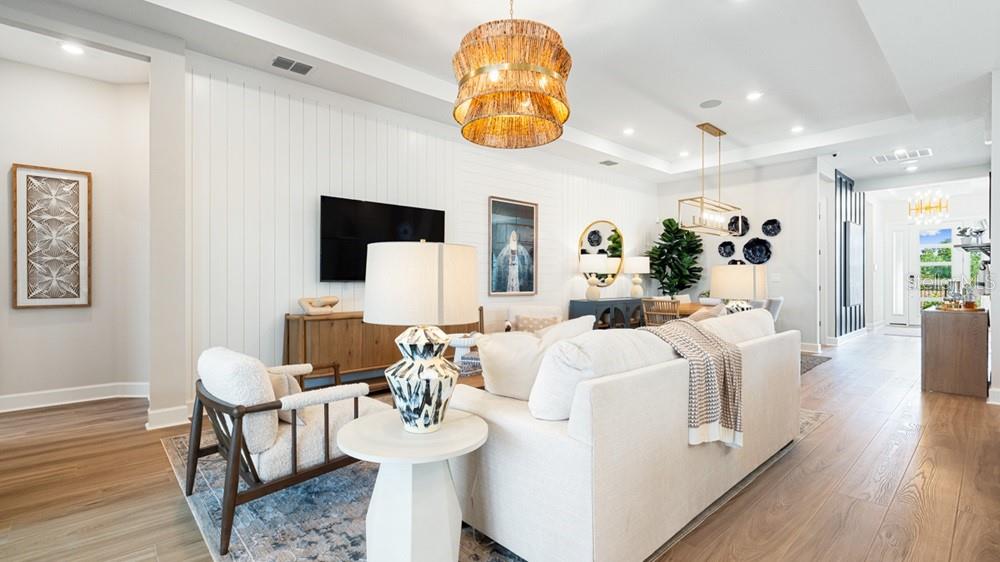 A bright living room features a white sofa, wood-paneled walls, and a large woven chandelier — 7420 MOONBEAM AVENUE, SARASOTA, FL