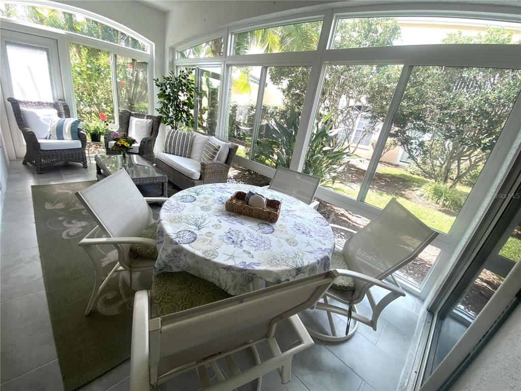 A sunroom features a dining table, wicker seating, and large windows overlooking a landscaped yard — 801 GONDOLA PARK DRIVE UNIT 801, VENICE, FL