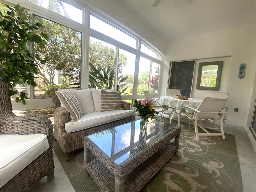A sunroom features wicker furniture, a glass-topped coffee table, and large windows overlooking greenery — 801 GONDOLA PARK DRIVE UNIT 801, VENICE, FL