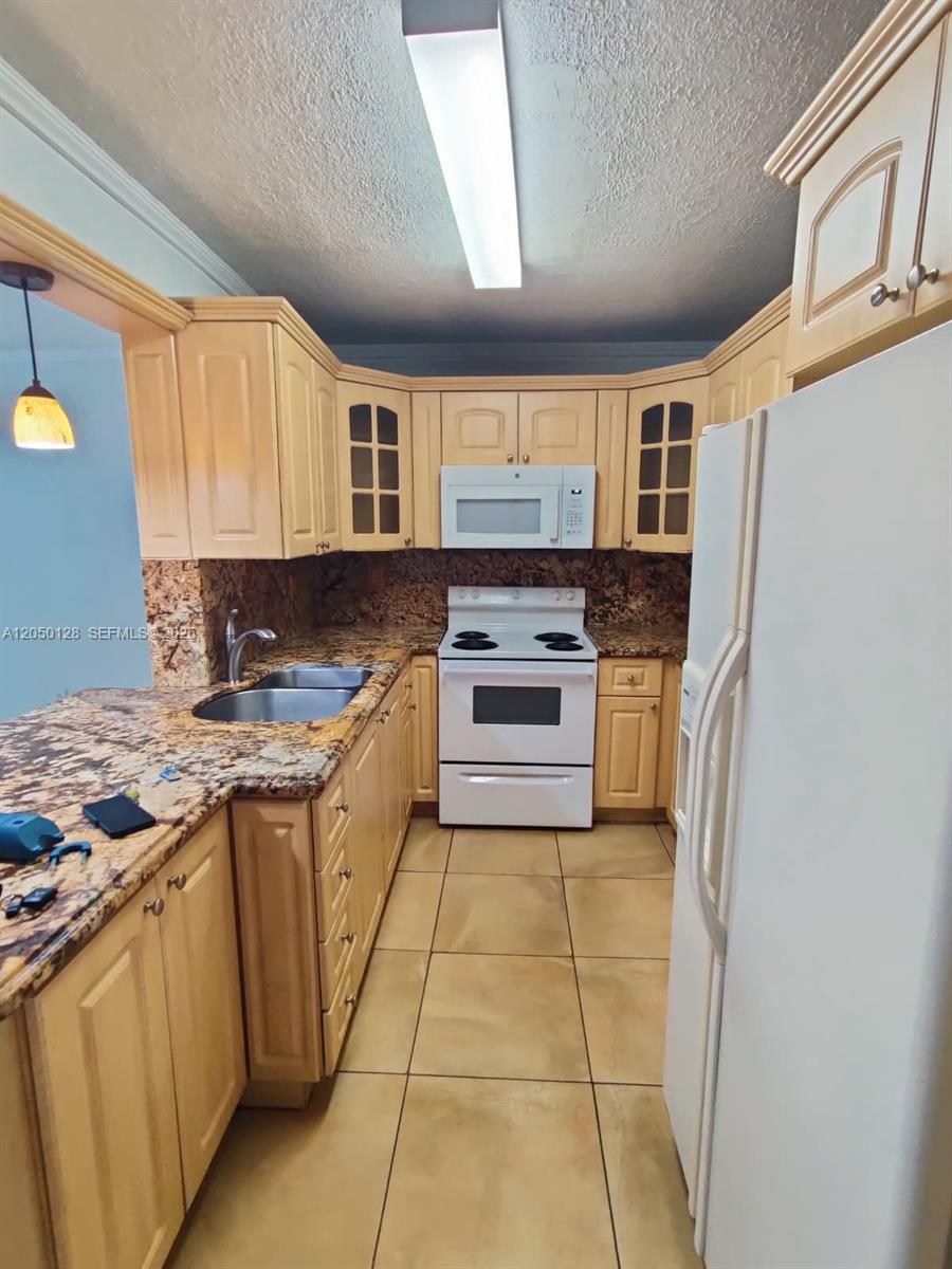 A kitchen features light wood cabinets, granite countertops, white appliances, and beige tile flooring — 5705 W 20th Ave # 215, Hialeah FL 33012, HIALEAH, FL