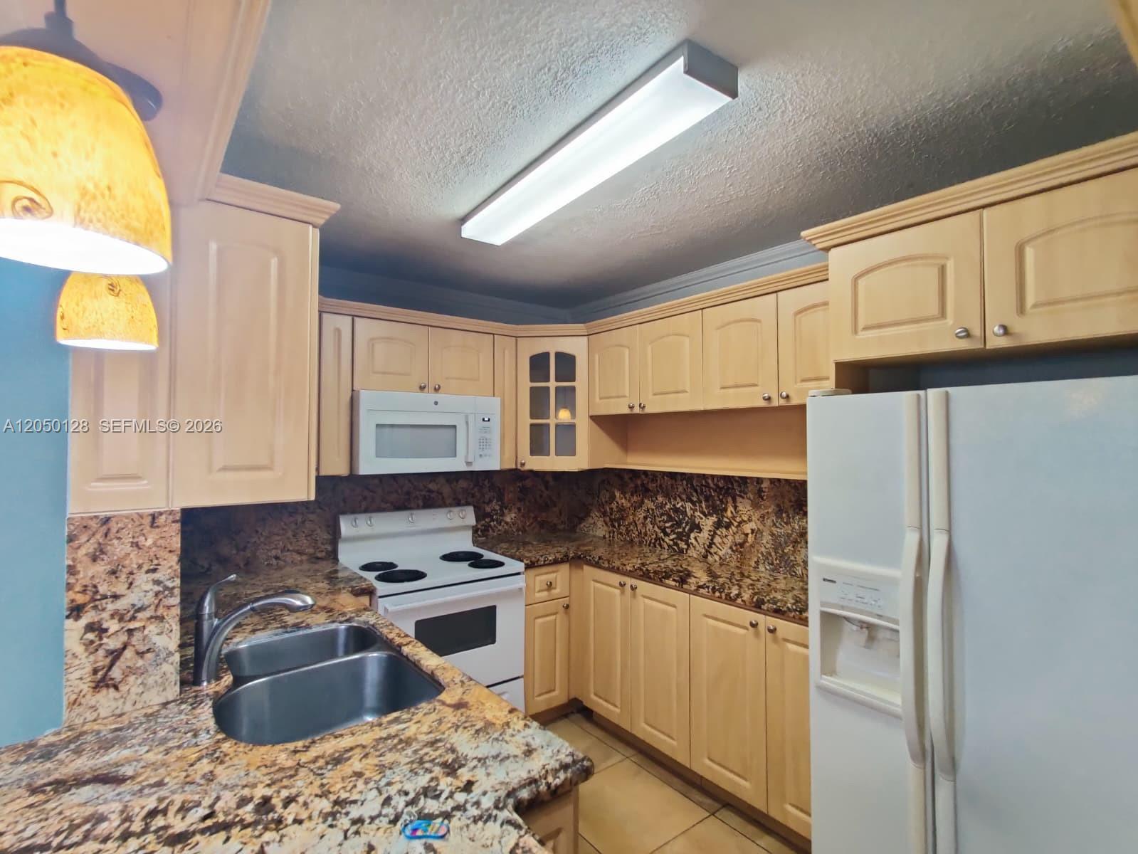A kitchen features light wood cabinets, granite countertops, a white stove, and a white refrigerator — 5705 W 20th Ave # 215, Hialeah FL 33012, HIALEAH, FL