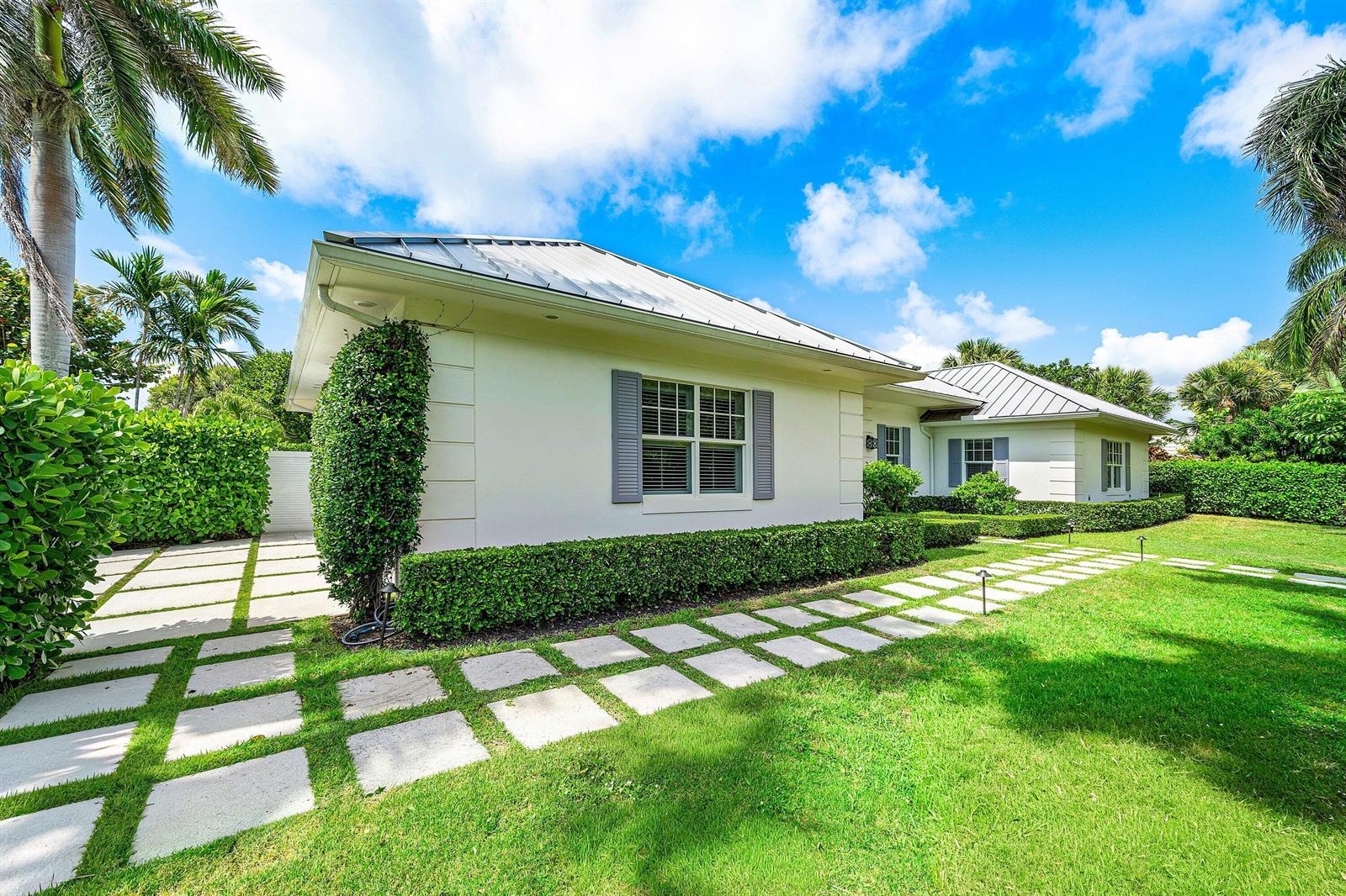 A white house with a metal roof and stone paver walkway sits on a lawn — 106 Beachway Drive, Ocean Ridge FL 33435, OCEAN RIDGE, FL
