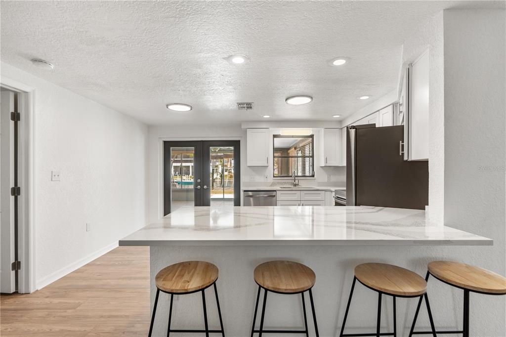 A kitchen with white cabinets, a quartz island, and bar stools overlooks a patio area — 13912 DARLENE AVENUE, HUDSON, FL