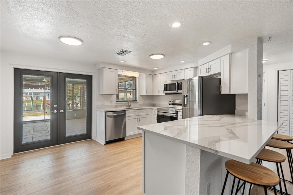 A kitchen with white cabinets, stainless steel appliances, a quartz island, and light wood flooring — 13912 DARLENE AVENUE, HUDSON, FL