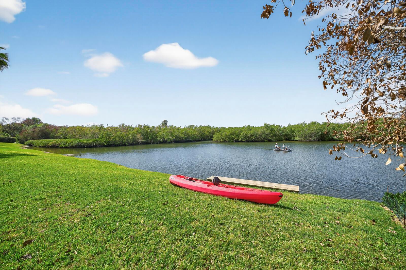 A red kayak sits on a grassy lawn beside a lake with a small boat — VERO BEACH, FL