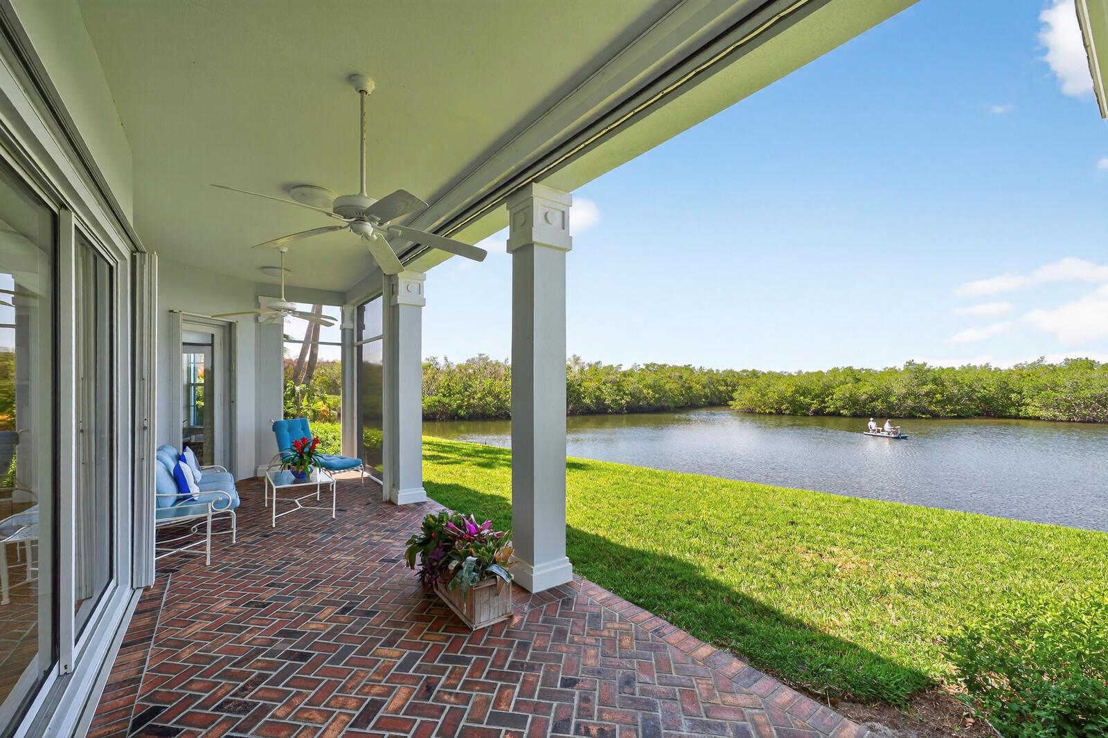 A covered brick patio overlooks a grassy lawn and a canal with a small boat — VERO BEACH, FL
