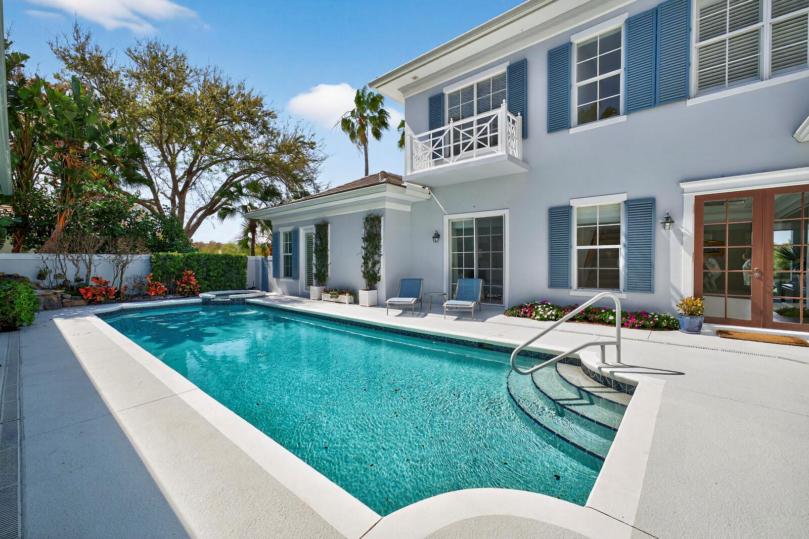 A swimming pool with steps and a handrail sits in front of a blue house — VERO BEACH, FL