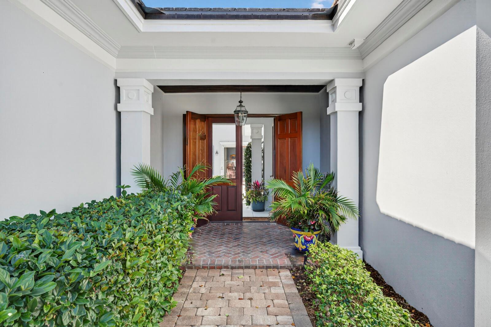 A brick walkway leads to an open wooden front door framed by white columns — VERO BEACH, FL