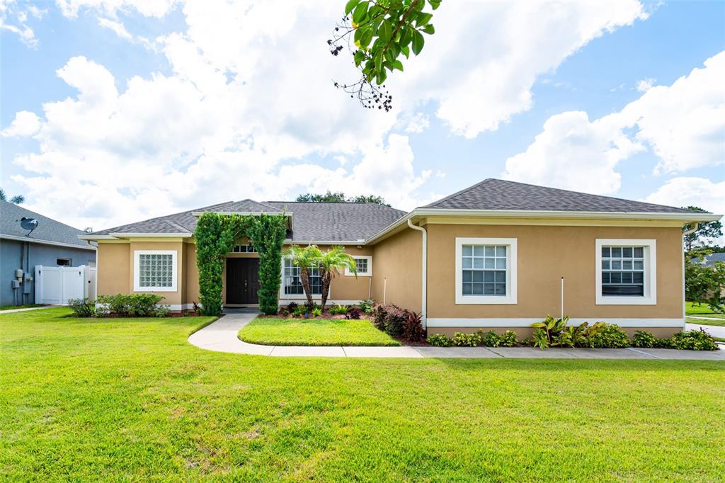 A tan single-story house with a brown garage door sits on a grassy corner lot — 1643 SHONNORA DRIVE, GOTHA, FL