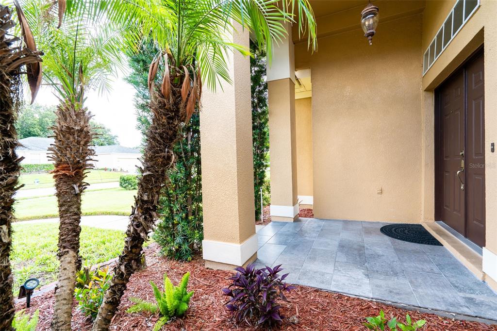 A covered entryway features a tiled porch, a dark double door, and palm trees — 1643 SHONNORA DRIVE, GOTHA, FL