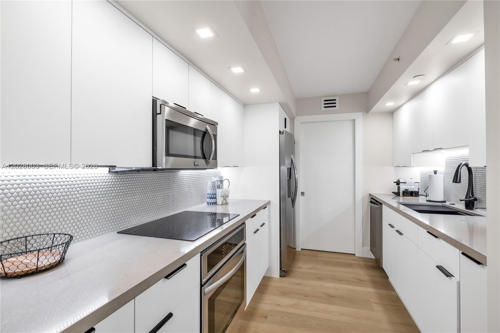 A modern galley kitchen features white cabinets, stainless steel appliances, and a tiled backsplash — 6917 Collins Ave # 1404, Miami Beach FL 33141, MIAMI BEACH, FL