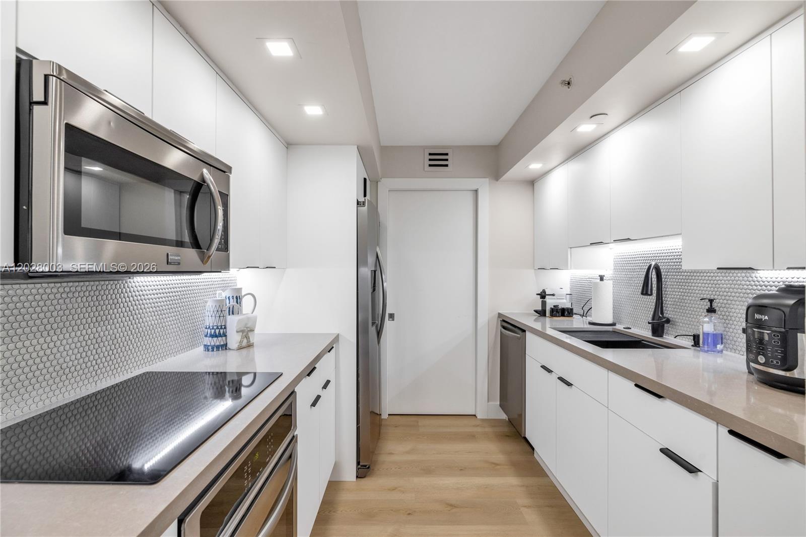 A galley kitchen features white cabinets, stainless steel appliances, and a light-colored tile backsplash — 6917 Collins Ave # 1404, Miami Beach FL 33141, MIAMI BEACH, FL