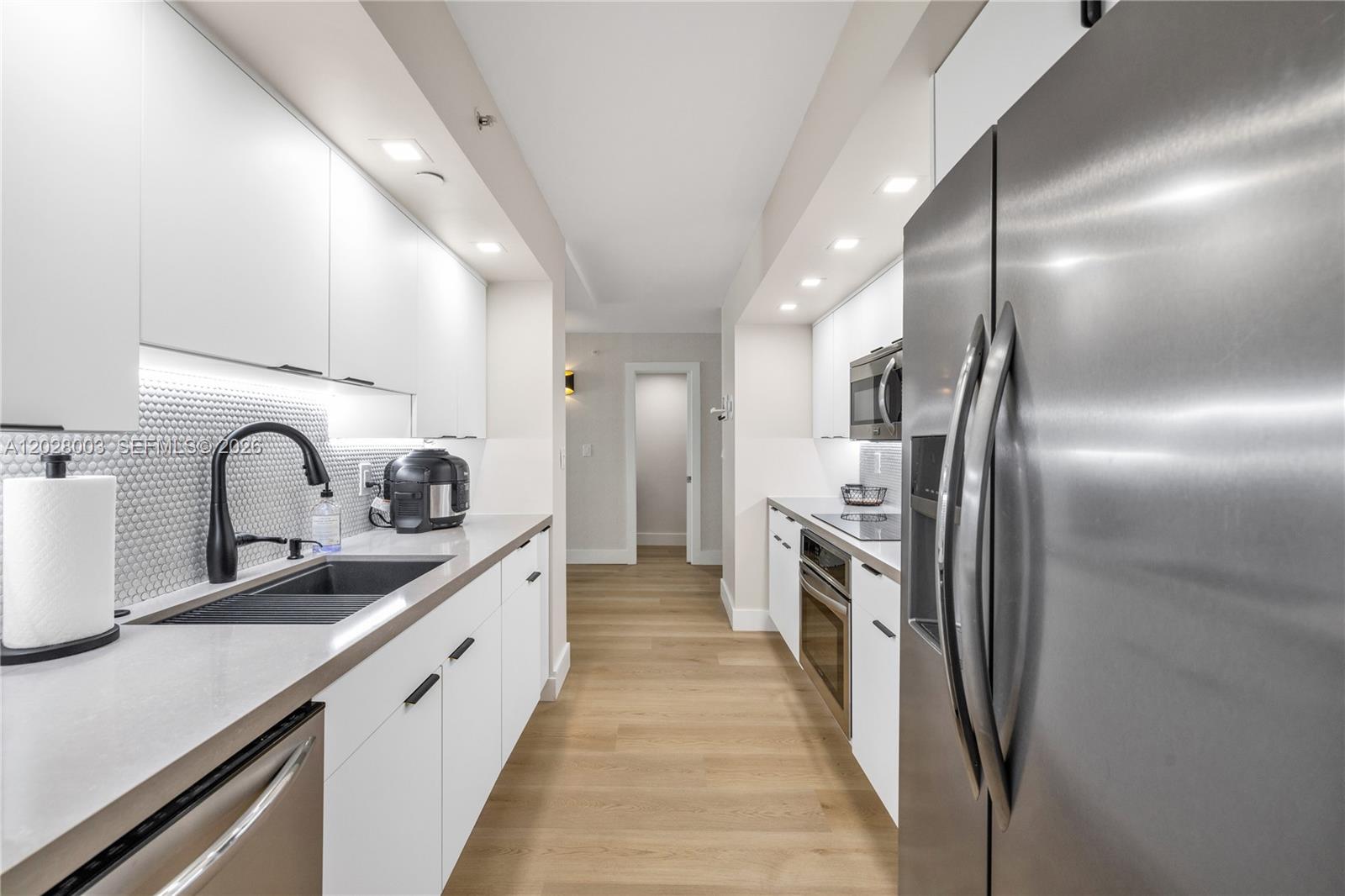 A galley kitchen features white cabinets, stainless steel appliances, and light wood flooring — 6917 Collins Ave # 1404, Miami Beach FL 33141, MIAMI BEACH, FL
