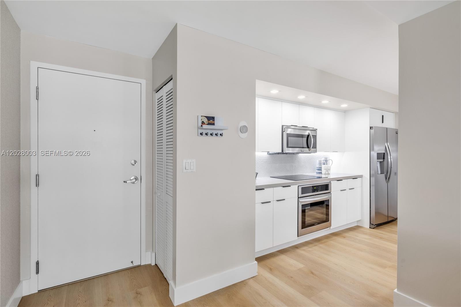 A modern kitchen features white cabinets, stainless steel appliances, and light wood flooring — 6917 Collins Ave # 1404, Miami Beach FL 33141, MIAMI BEACH, FL