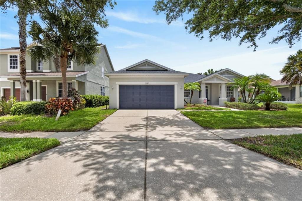 A single-story house with a gray garage door, concrete driveway, and landscaped front yard — 11023 HOLLY CONE DRIVE, RIVERVIEW, FL