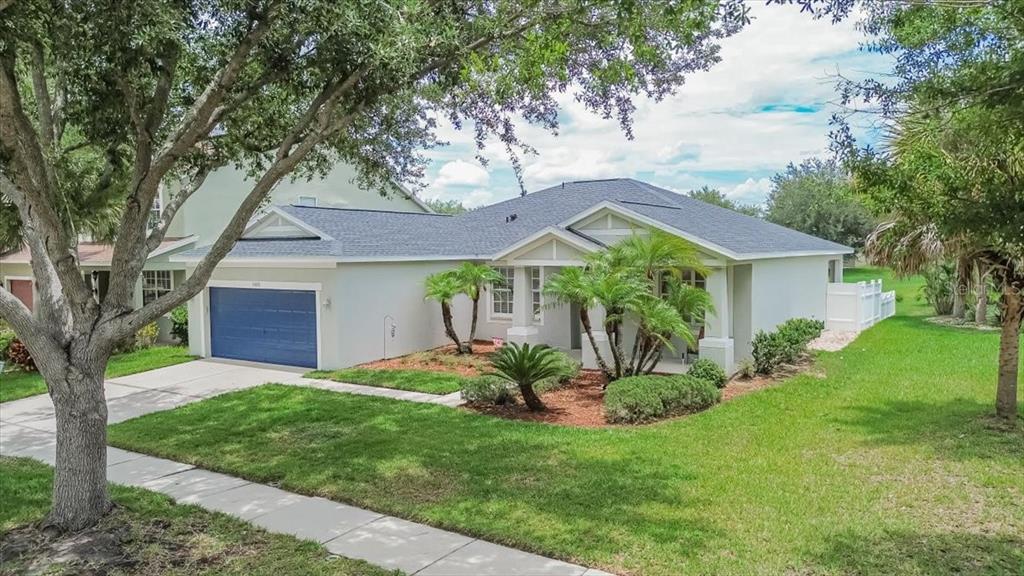 A single-story house with a blue garage door, light-colored stucco exterior, and landscaped front yard — 11023 HOLLY CONE DRIVE, RIVERVIEW, FL