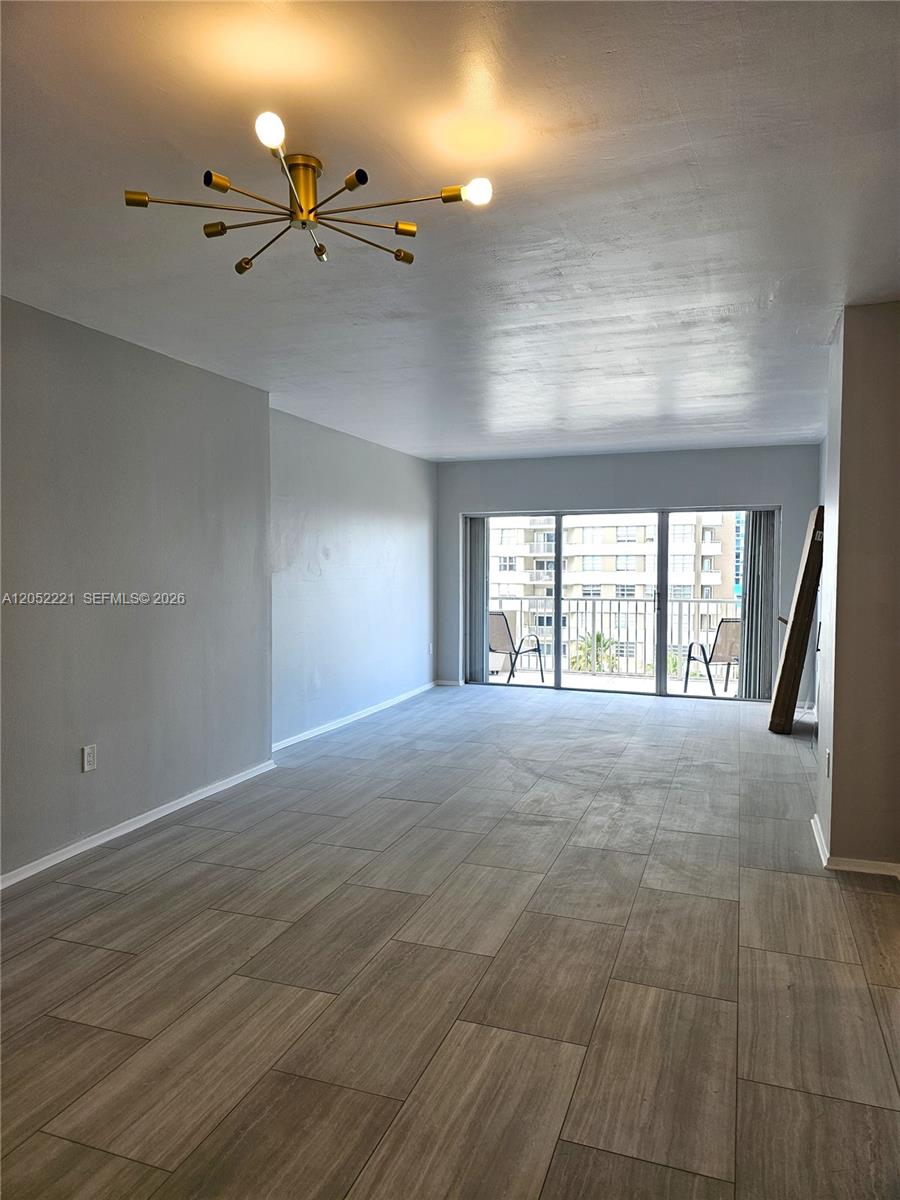 An empty living room features gray tile flooring, a modern chandelier, and a balcony with outdoor seating — 1985 S Ocean Dr # 5D, Hallandale Beach FL 33009, HALLANDALE BEACH, FL
