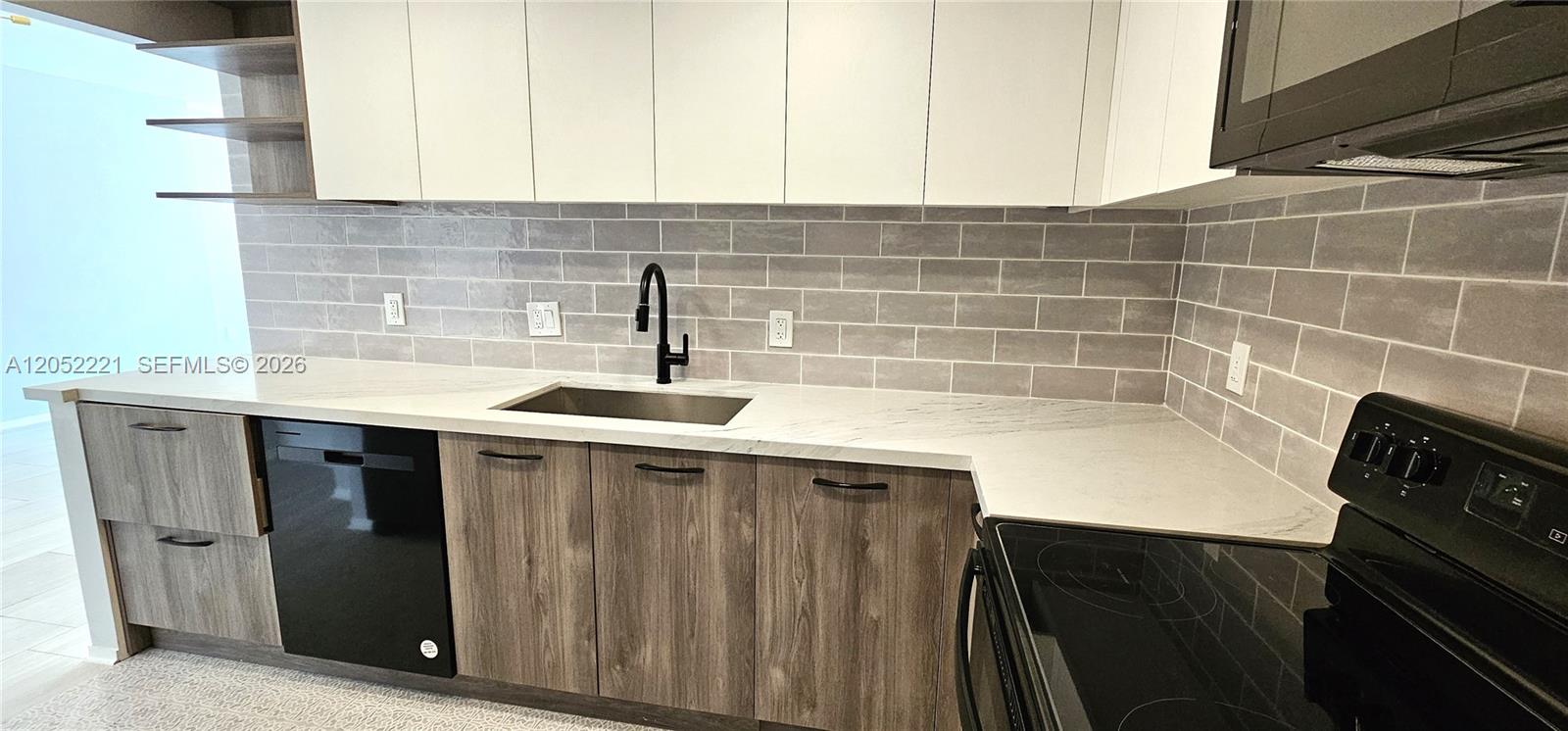 A modern kitchen features white upper cabinets, wood-grain lower cabinets, and a gray subway tile backsplash — 1985 S Ocean Dr # 5D, Hallandale Beach FL 33009, HALLANDALE BEACH, FL