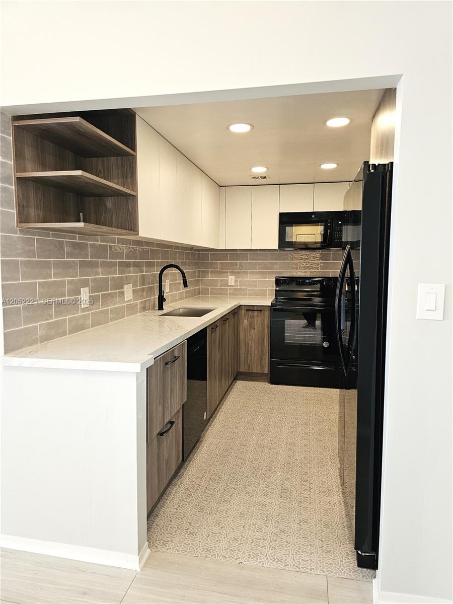 A galley kitchen features wood-grain lower cabinets, white upper cabinets, and a gray tiled backsplash — 1985 S Ocean Dr # 5D, Hallandale Beach FL 33009, HALLANDALE BEACH, FL