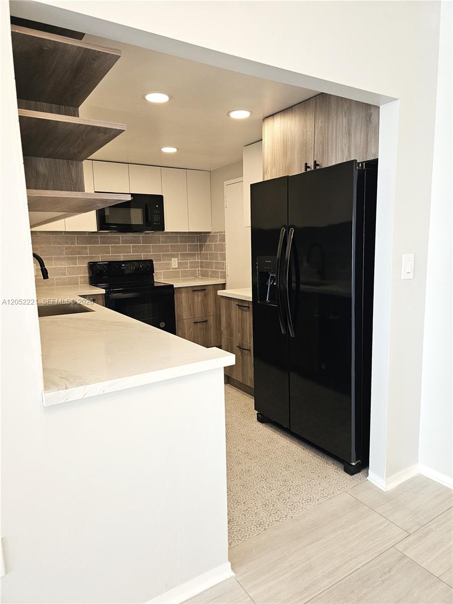 A kitchen features wood-grain cabinets, white countertops, a black refrigerator, and a gray backsplash — 1985 S Ocean Dr # 5D, Hallandale Beach FL 33009, HALLANDALE BEACH, FL