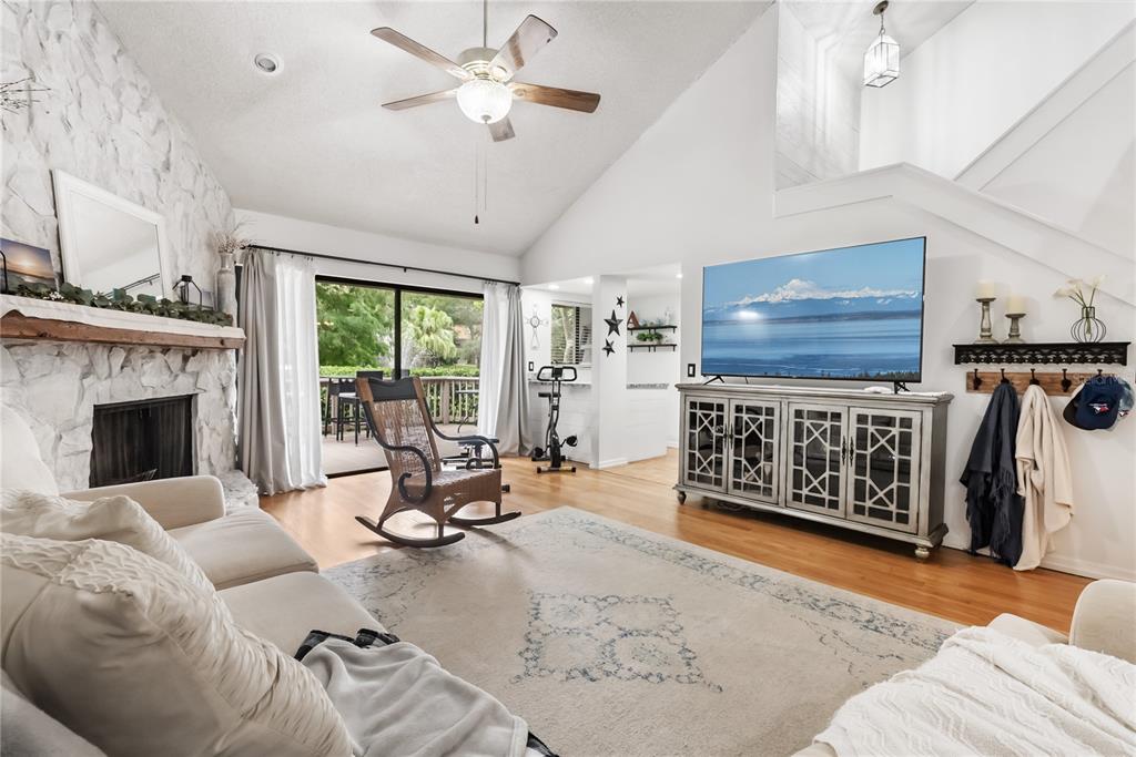A living room features a stone fireplace, vaulted ceiling, hardwood floors, and a sliding glass door — 303 OLD MILL POND ROAD UNIT 303, PALM HARBOR, FL