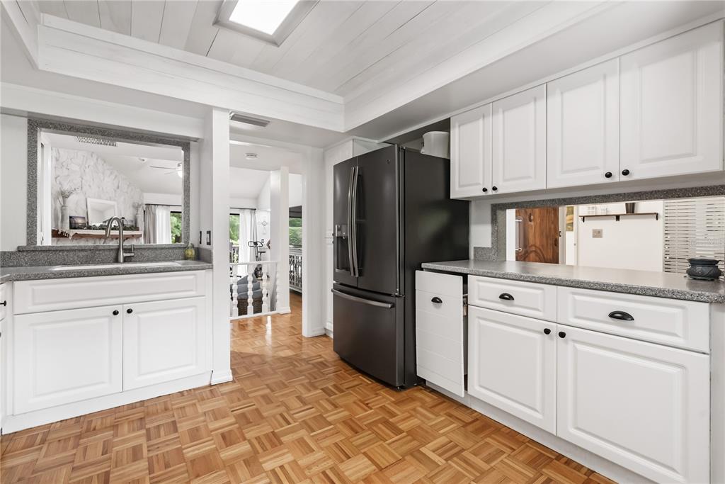 A kitchen features white cabinets, a black refrigerator, gray countertops, and parquet wood flooring — 303 OLD MILL POND ROAD UNIT 303, PALM HARBOR, FL