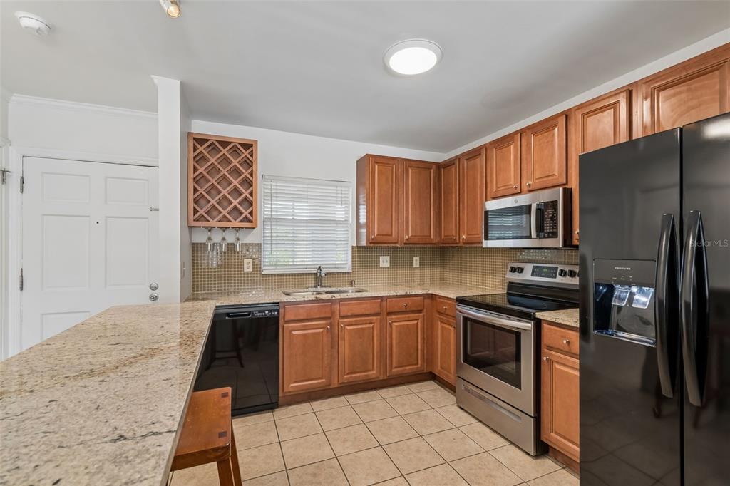 A kitchen features wood cabinets, granite countertops, stainless steel appliances, and a black refrigerator — 10314 CARROLLWOOD COURT UNIT 56, TAMPA, FL