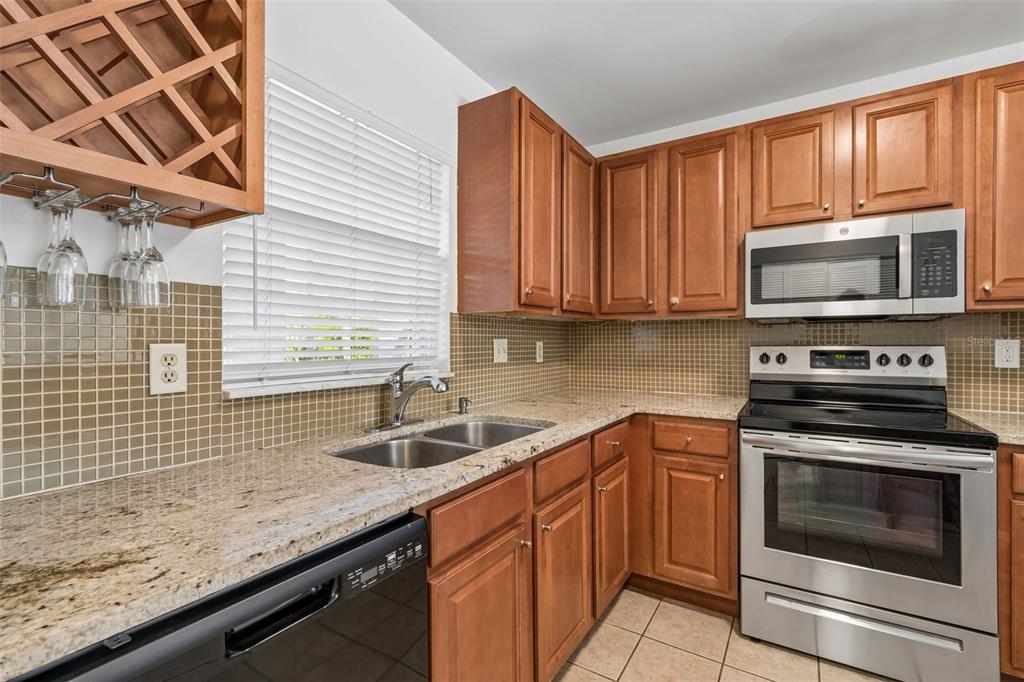 A kitchen with wood cabinets, granite countertops, stainless steel appliances, and a tiled backsplash — 10314 CARROLLWOOD COURT UNIT 56, TAMPA, FL