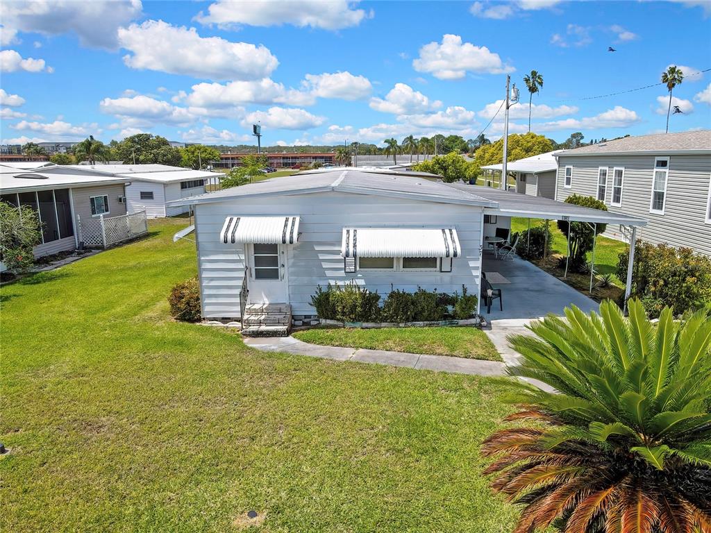 A white mobile home with a metal awning and a carport sits on a lawn — 37 WILLIAM PENN WAY UNIT 13, PALM HARBOR, FL