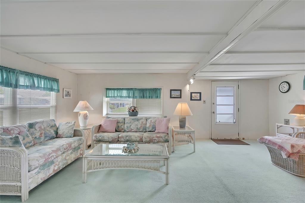 A living room features light green carpeting, white wicker furniture, floral sofas, and a white door — 37 WILLIAM PENN WAY UNIT 13, PALM HARBOR, FL