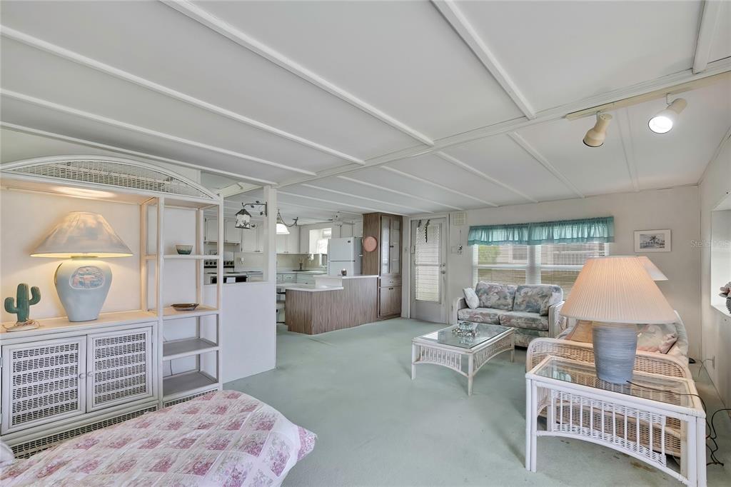 A living room with light green carpeting, white wicker furniture, and an open kitchen area — 37 WILLIAM PENN WAY UNIT 13, PALM HARBOR, FL