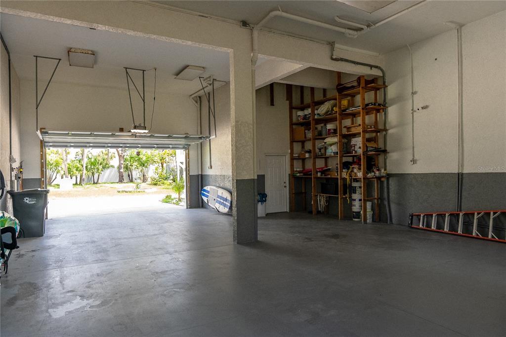 A spacious, unfinished garage with a concrete floor, open shelving, and an open overhead door — 2424 BAY DRIVE UNIT 2424/2426, BRADENTON, FL