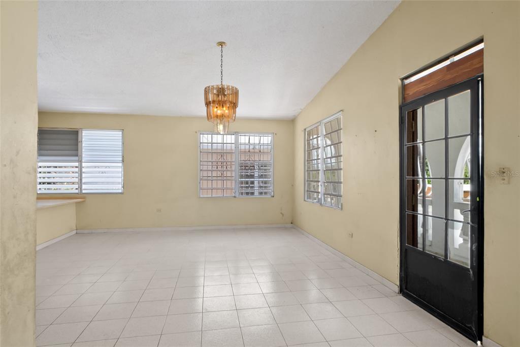 An empty room with white tile floors, yellow walls, a chandelier, and a glass door — 638 CALLE B COM. SERRANO, JUANA DIAZ, PR