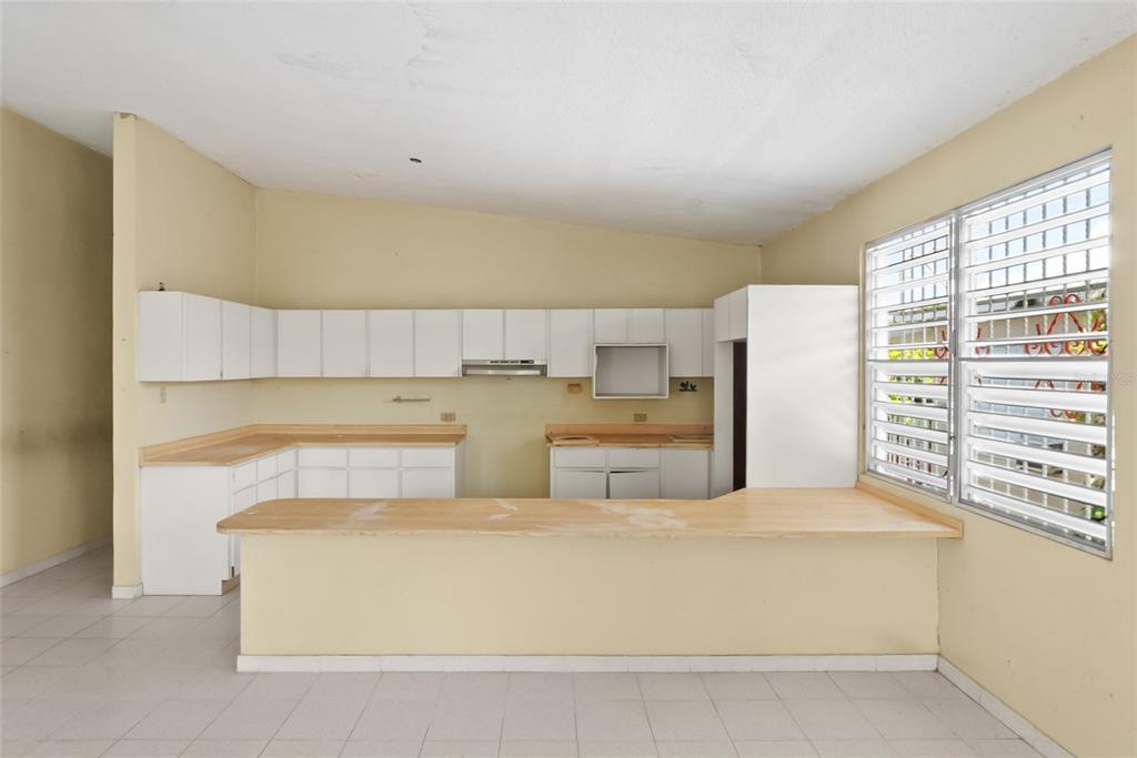 An empty kitchen features white cabinets, light-colored countertops, a breakfast bar, and jalousie windows — 638 CALLE B COM. SERRANO, JUANA DIAZ, PR