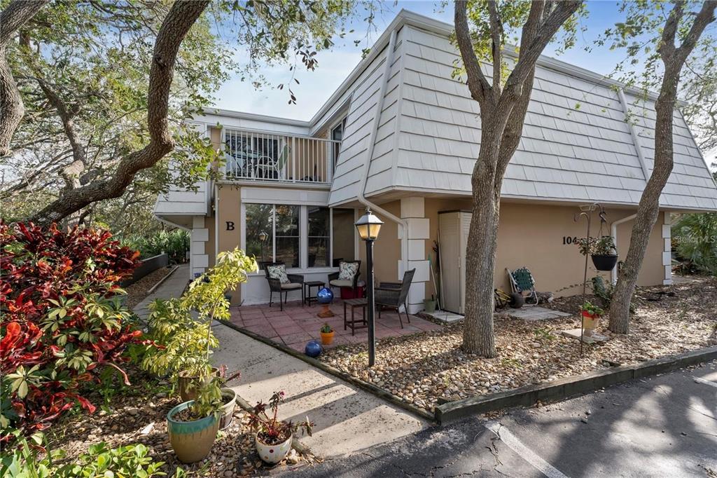 A two-story townhouse exterior features a tiled patio, a second-floor balcony, and surrounding trees — 4150 S ATLANTIC AVENUE UNIT 104 B, NEW SMYRNA BEACH, FL
