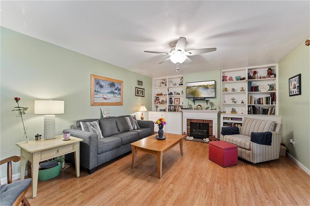 A living room features a gray sofa, a patterned armchair, a fireplace, and built-in shelving — 4150 S ATLANTIC AVENUE UNIT 104 B, NEW SMYRNA BEACH, FL