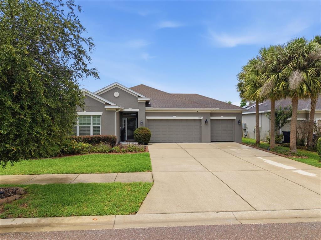 A single-story gray house with a three-car garage and a concrete driveway — 17735 BRIGHT WHEAT DRIVE, LITHIA, FL