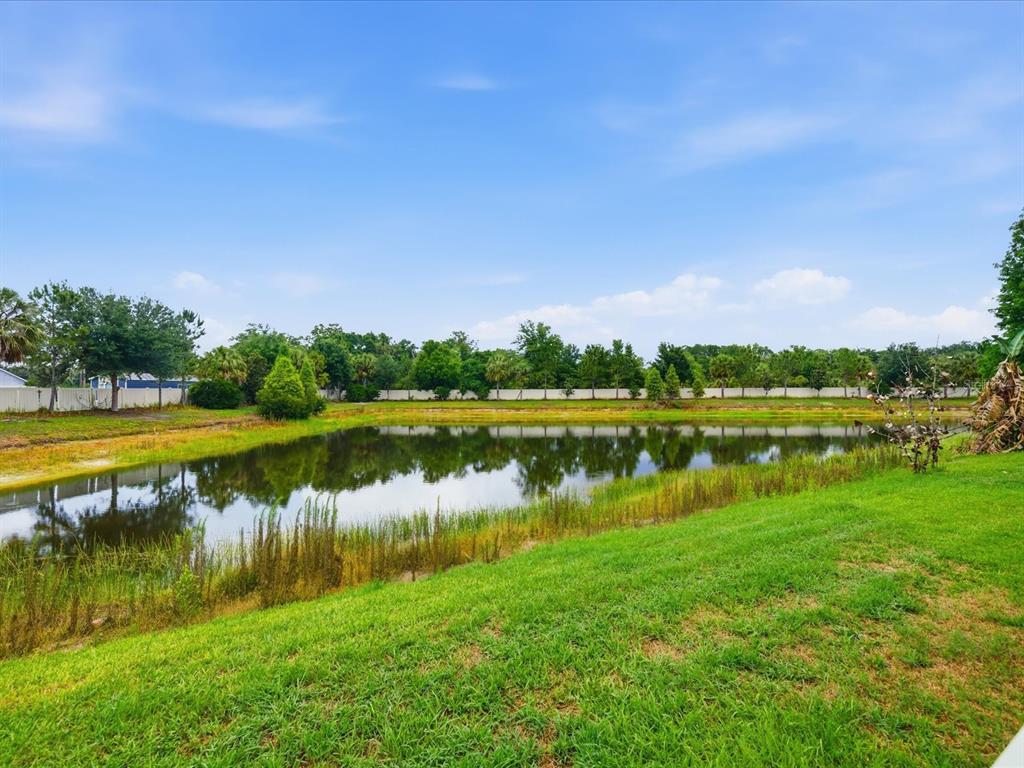 A grassy lawn slopes down toward a pond bordered by trees and a white fence — 17735 BRIGHT WHEAT DRIVE, LITHIA, FL