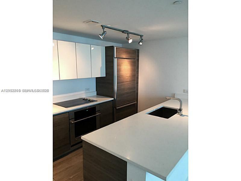 A modern kitchen features white upper cabinets, dark wood lower cabinets, and a white island — 1100 S Miami Ave # 411, Miami FL 33130, MIAMI, FL