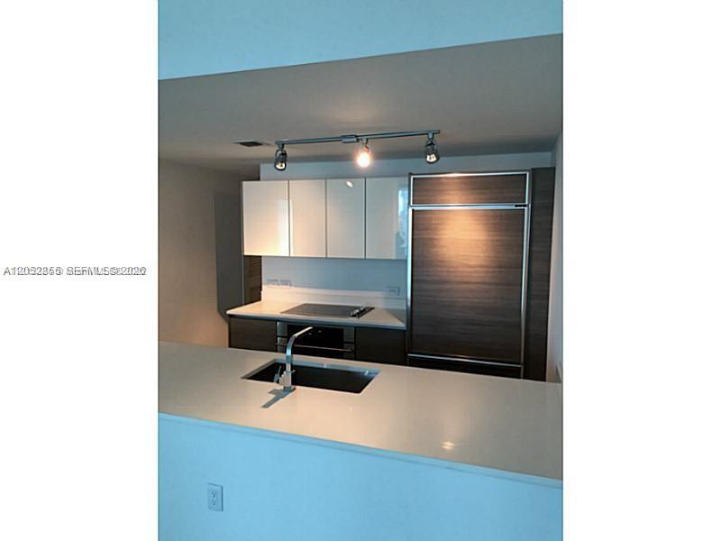 A modern kitchen features white upper cabinets, wood-paneled appliances, and a white countertop island — 1100 S Miami Ave # 411, Miami FL 33130, MIAMI, FL